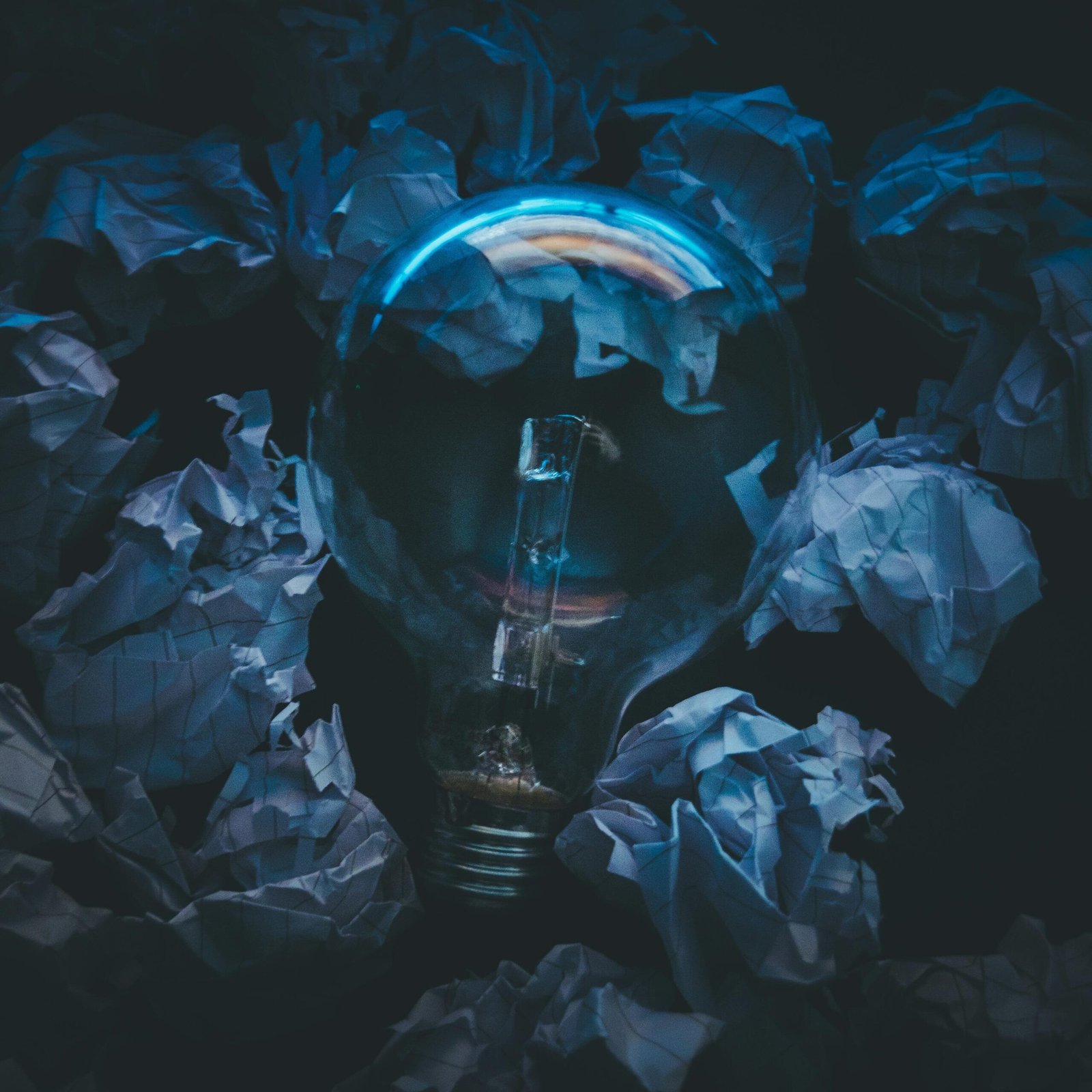 A light bulb surrounded by crumpled paper symbolizes creative ideas and innovation in a dark setting.